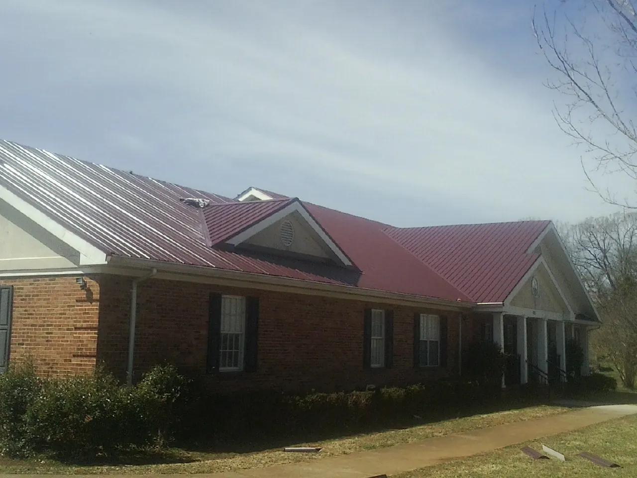 Red metal roof with gabled entries on a long brick building, from a Hail Damage Roof Repair job in Cedar Springs