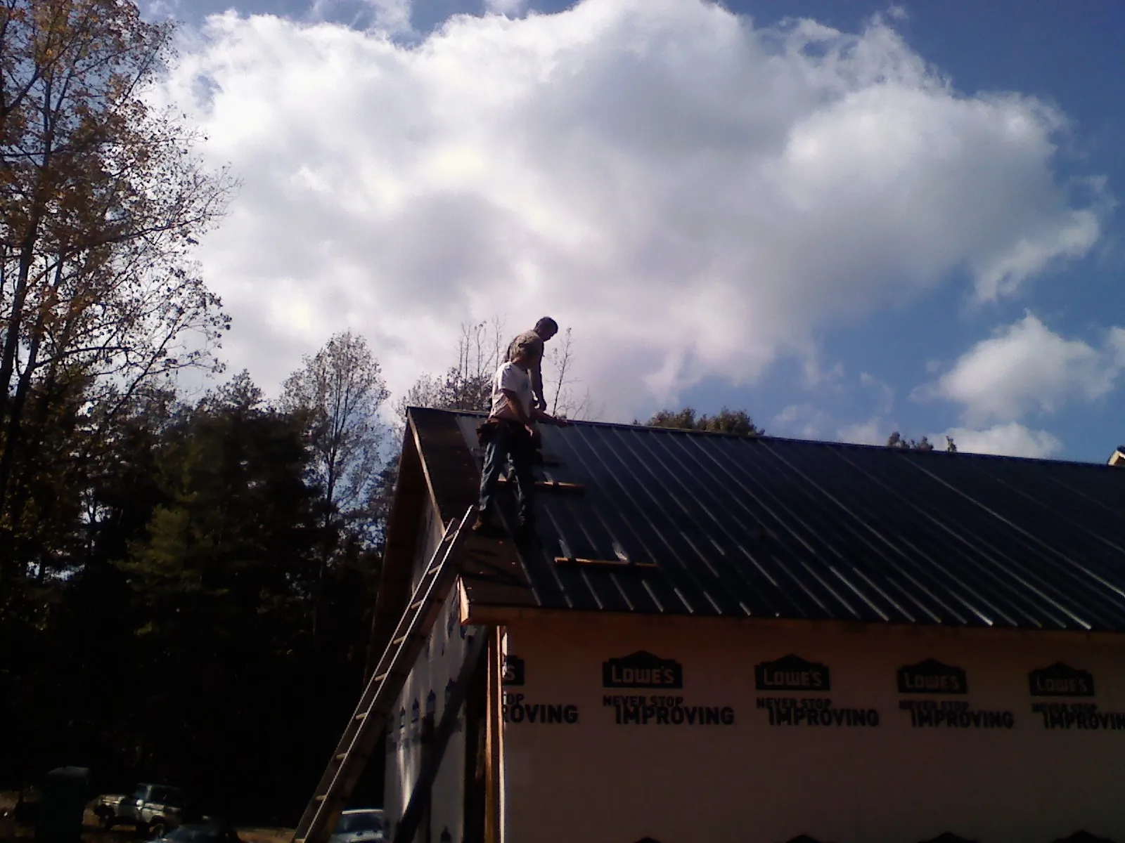 Roofer fastening dark metal panels high against a cloudy sky, from a Roof Inspection job in Cedar Springs