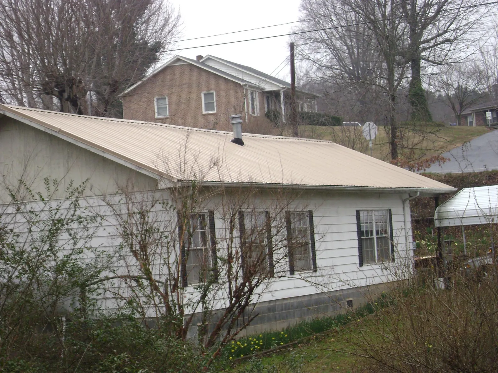 Tan metal roof on a white sided house set into a hillside — Commercial Roofing by Roofing Brothers in Cedar Springs