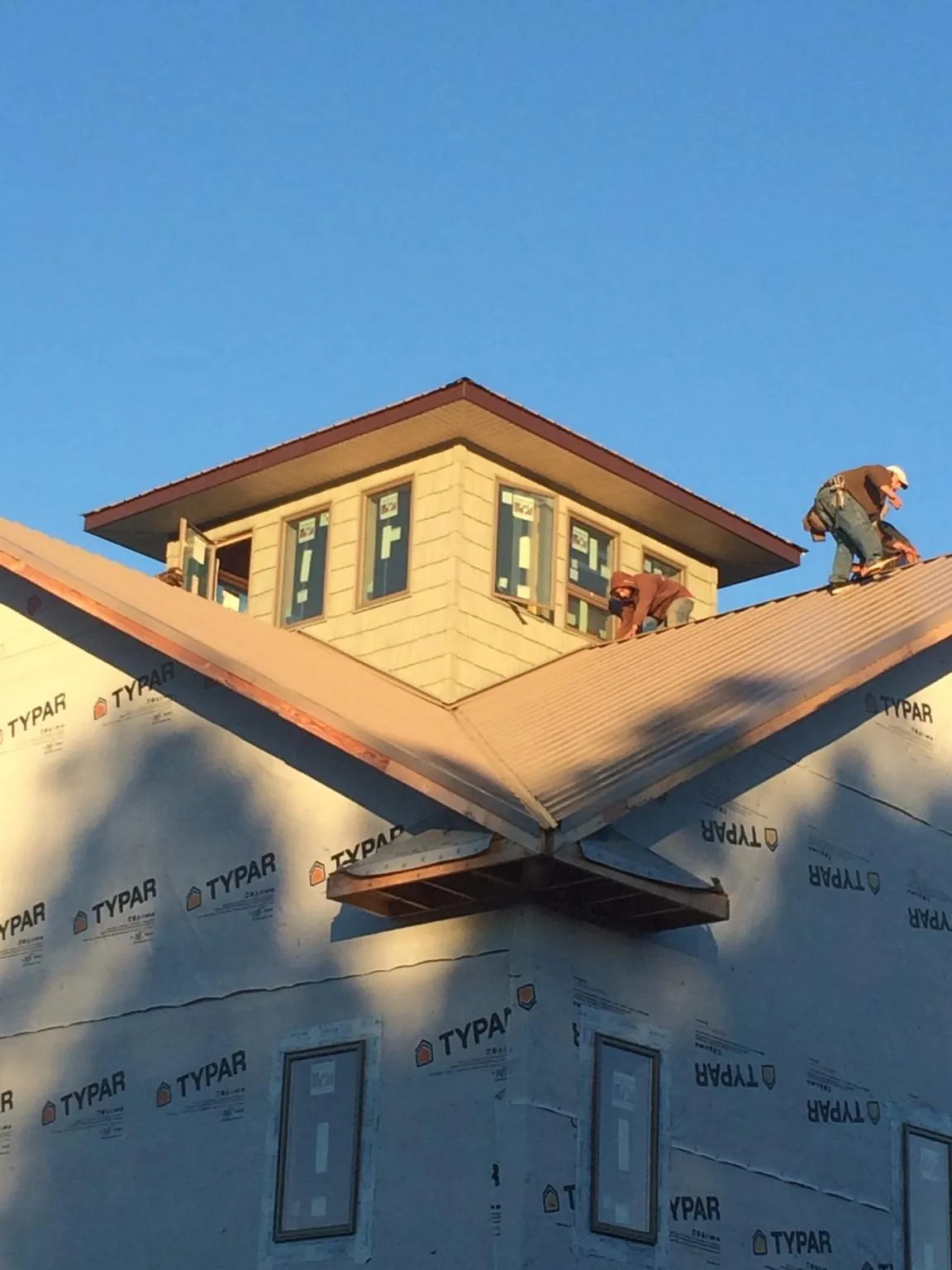 Roofers working around a rooftop cupola on a new metal roof at sunset in Cedar Springs